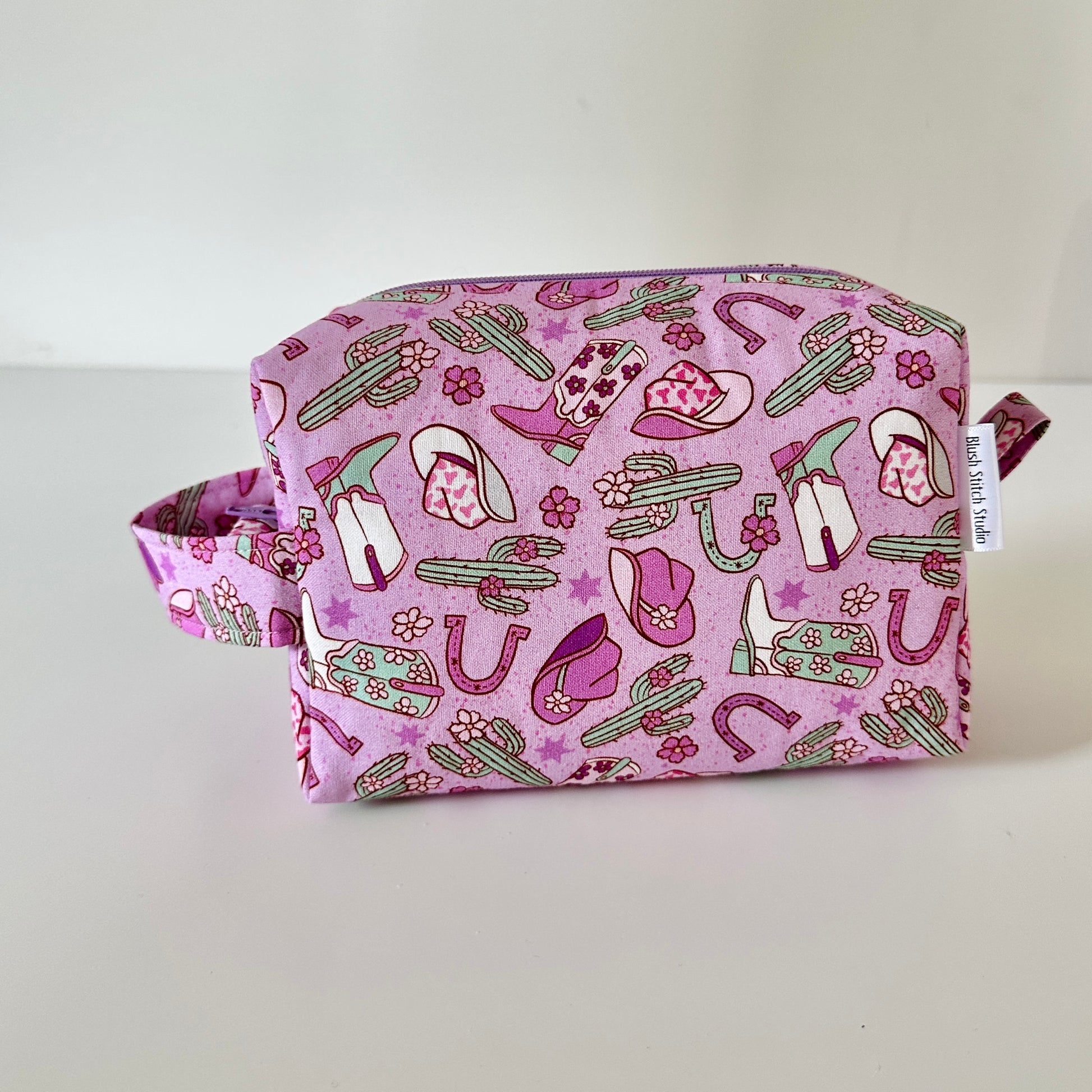Pink fabric pouch with cowboy pattern on a light gray background