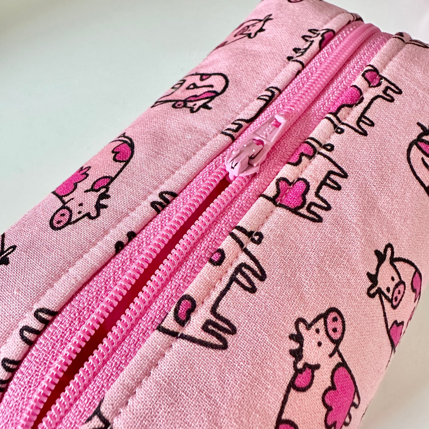 Pink pouch with cow pattern and zipper on a light gray background