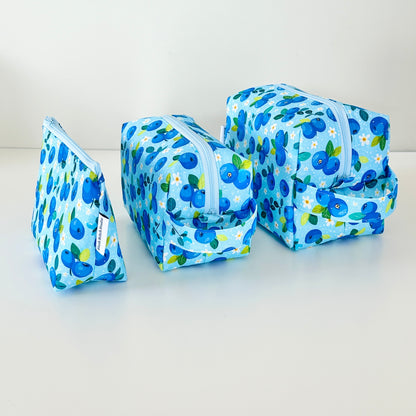 Set of three blue floral-patterned cosmetic makeup bags on a white background