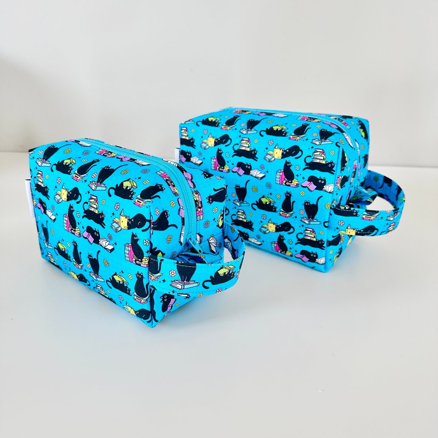 Two blue toiletry bags with black cat pattern on a white background