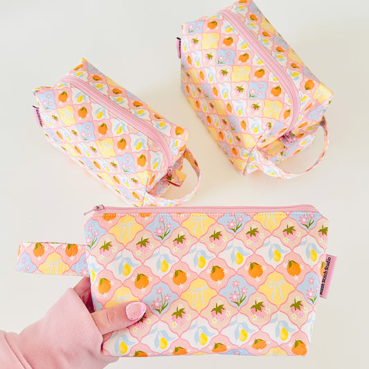 Set of three pink pouches with fruit pattern on a white background