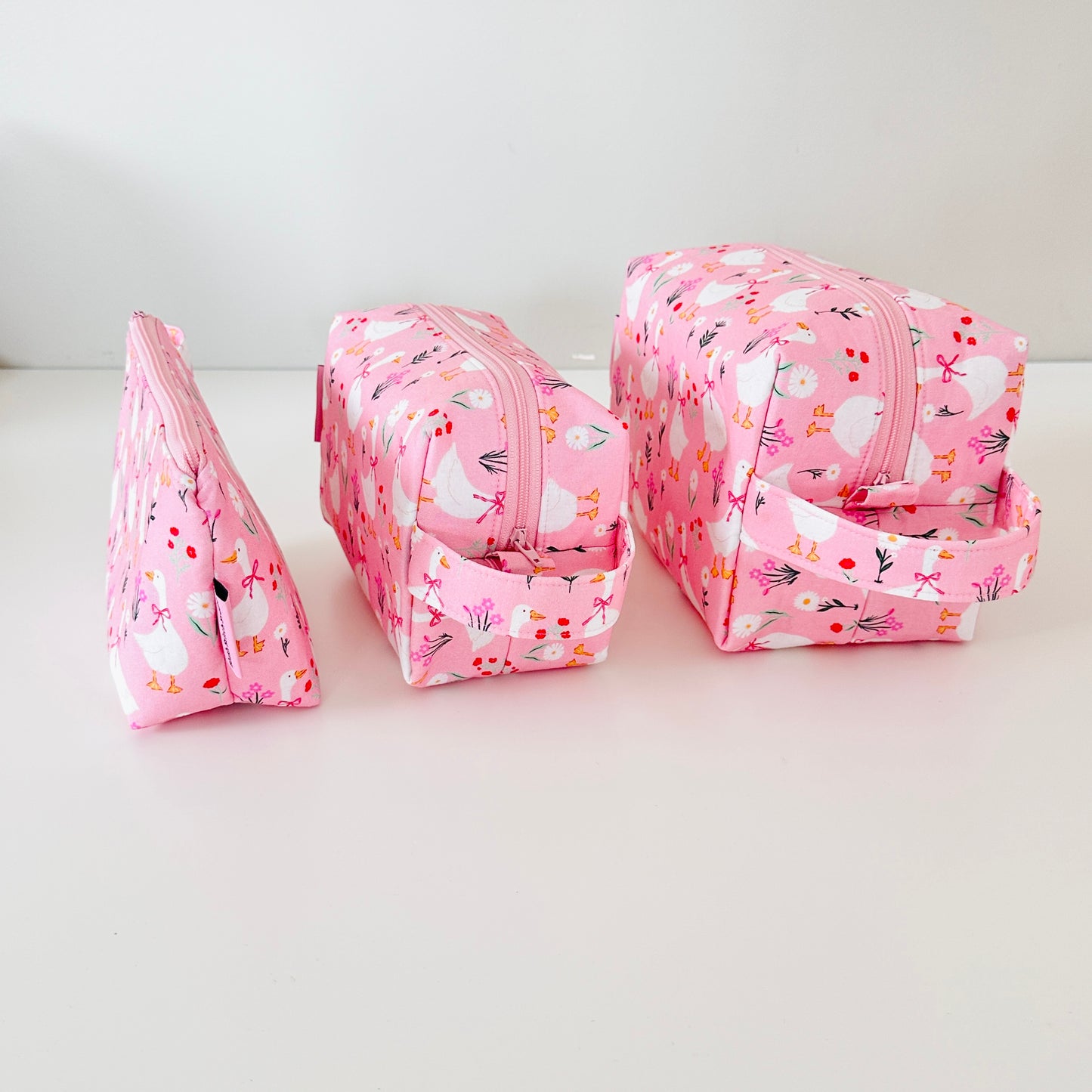 Set of three pink floral-patterned cosmetic bags on a white background