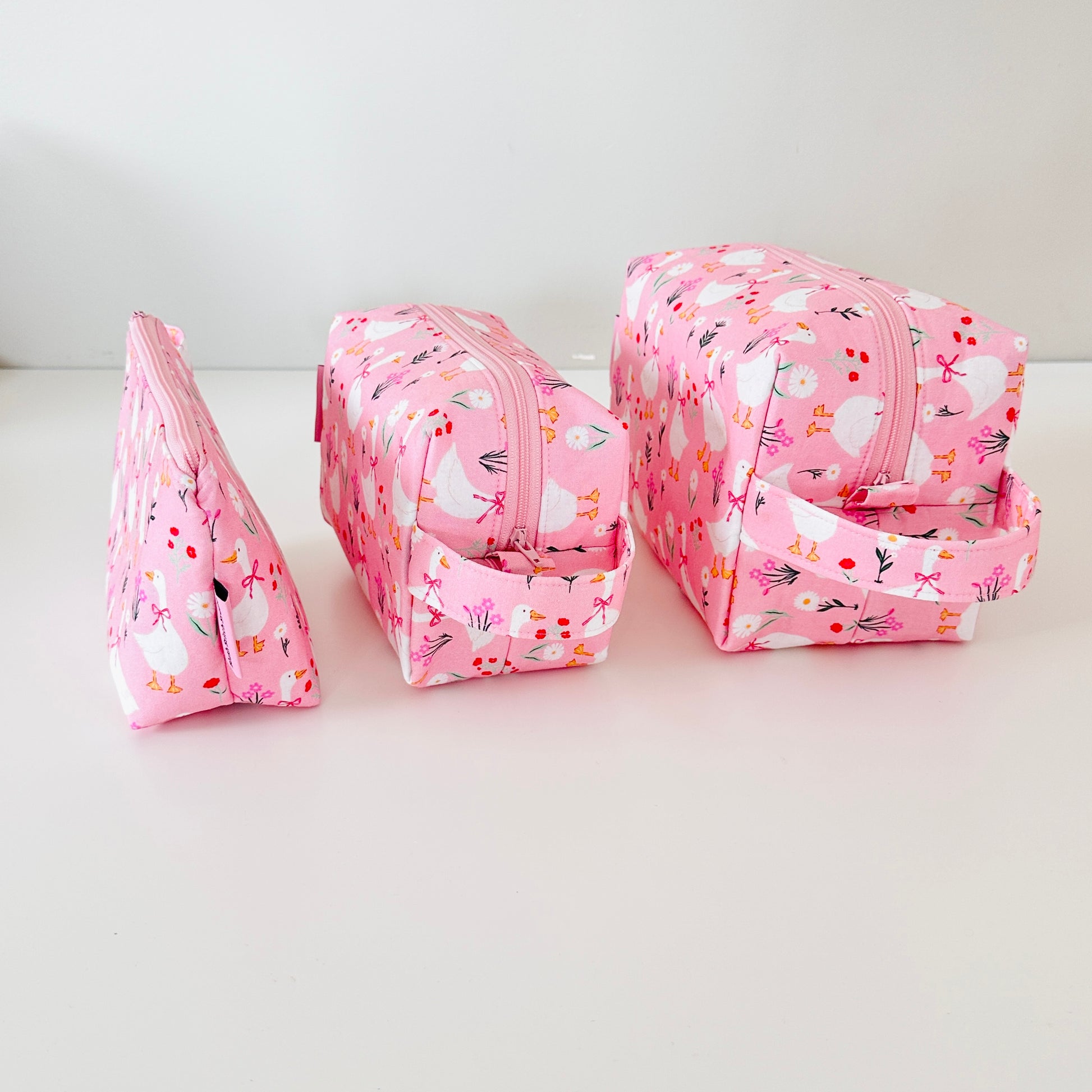 Set of three pink floral-patterned cosmetic bags on a white background