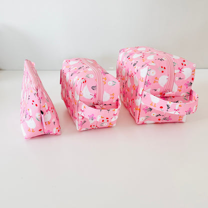 Set of three pink floral-patterned cosmetic bags on a white background