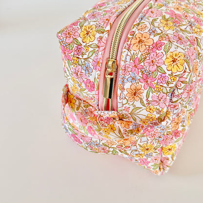 Floral patterned cosmetic bag with a gold zipper on a light gray background