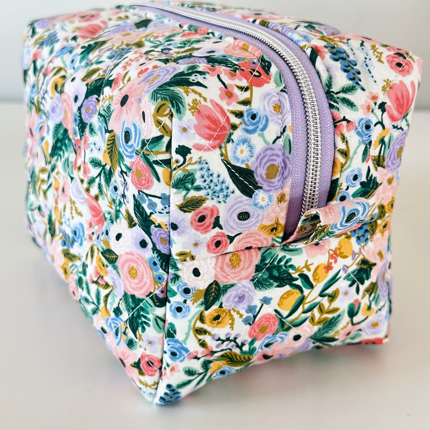 Floral patterned toiletry bag with a purple zipper on a light background