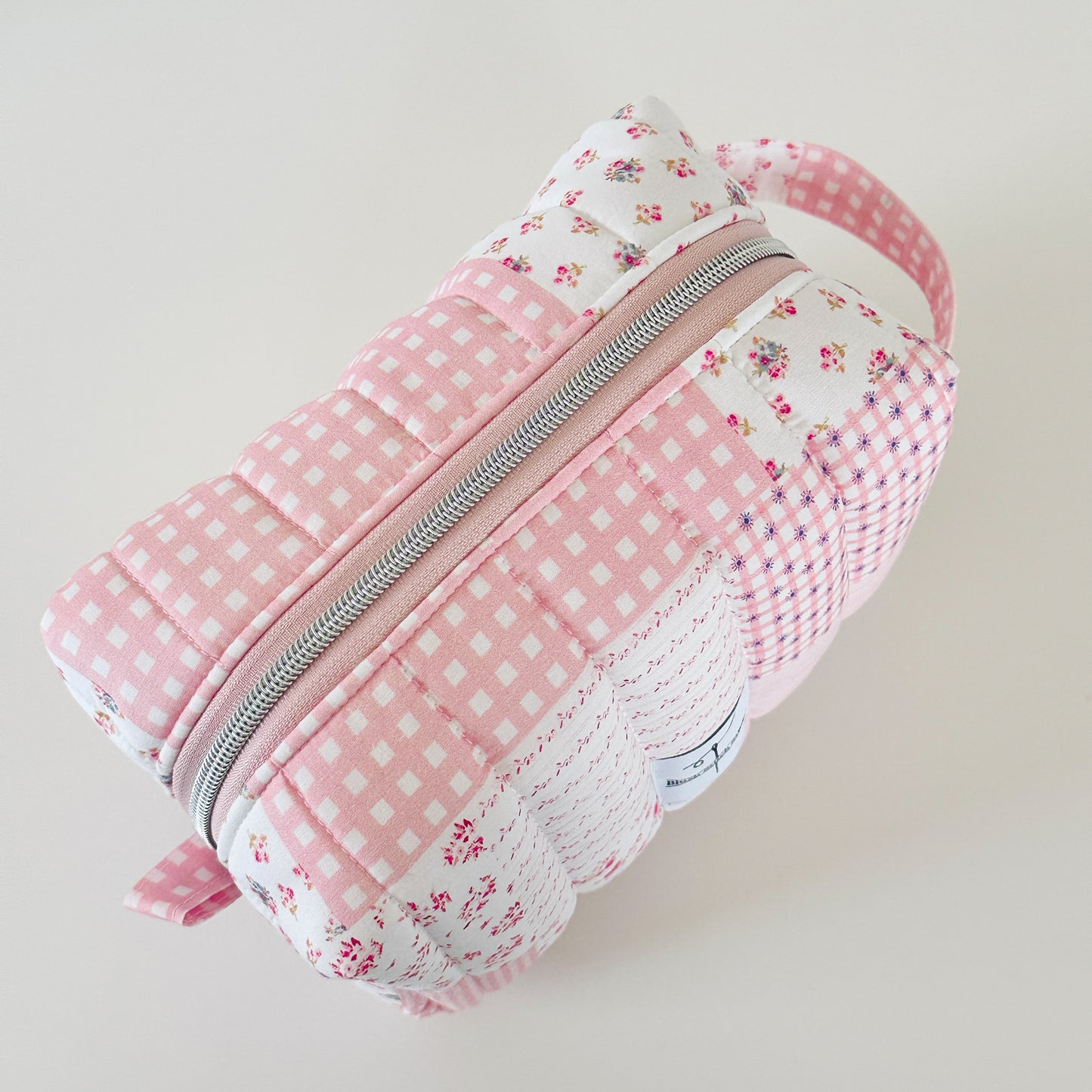 Pink and white checkered pouch with floral patterns on a light background