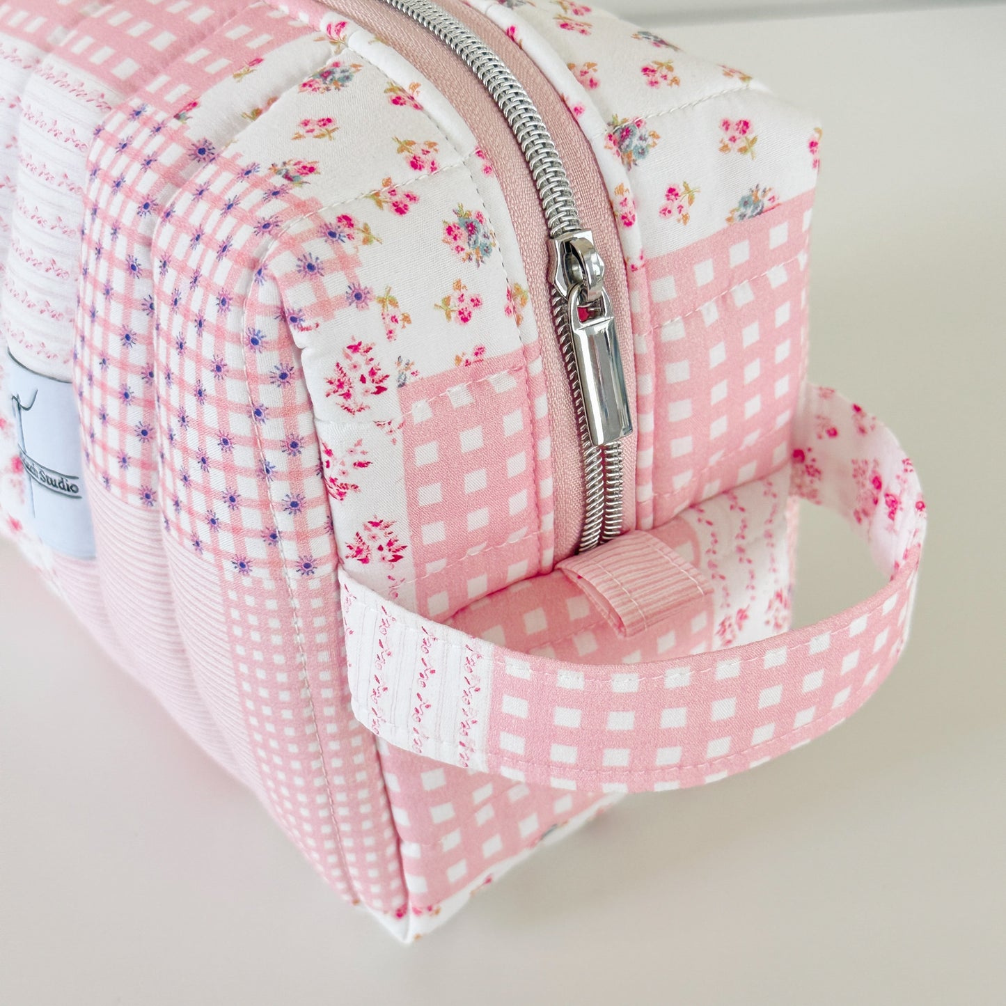 Pink floral and checkered patterned pouch with a zipper on a light background