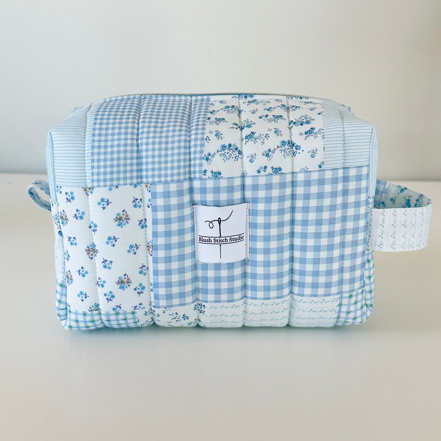 Quilted fabric makeup cosmetic  bag with blue checkered and floral patterns on a light gray background