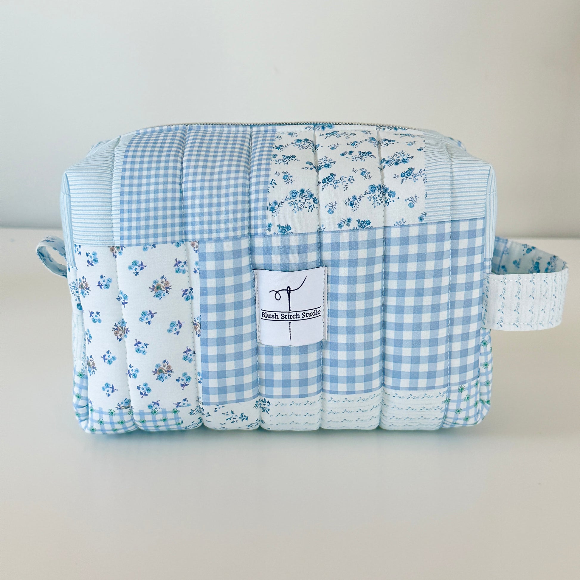 Quilted fabric makeup cosmetic  bag with blue checkered and floral patterns on a light gray background