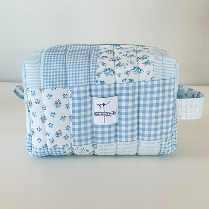 Quilted fabric makeup cosmetic  bag with blue checkered and floral patterns on a light gray background