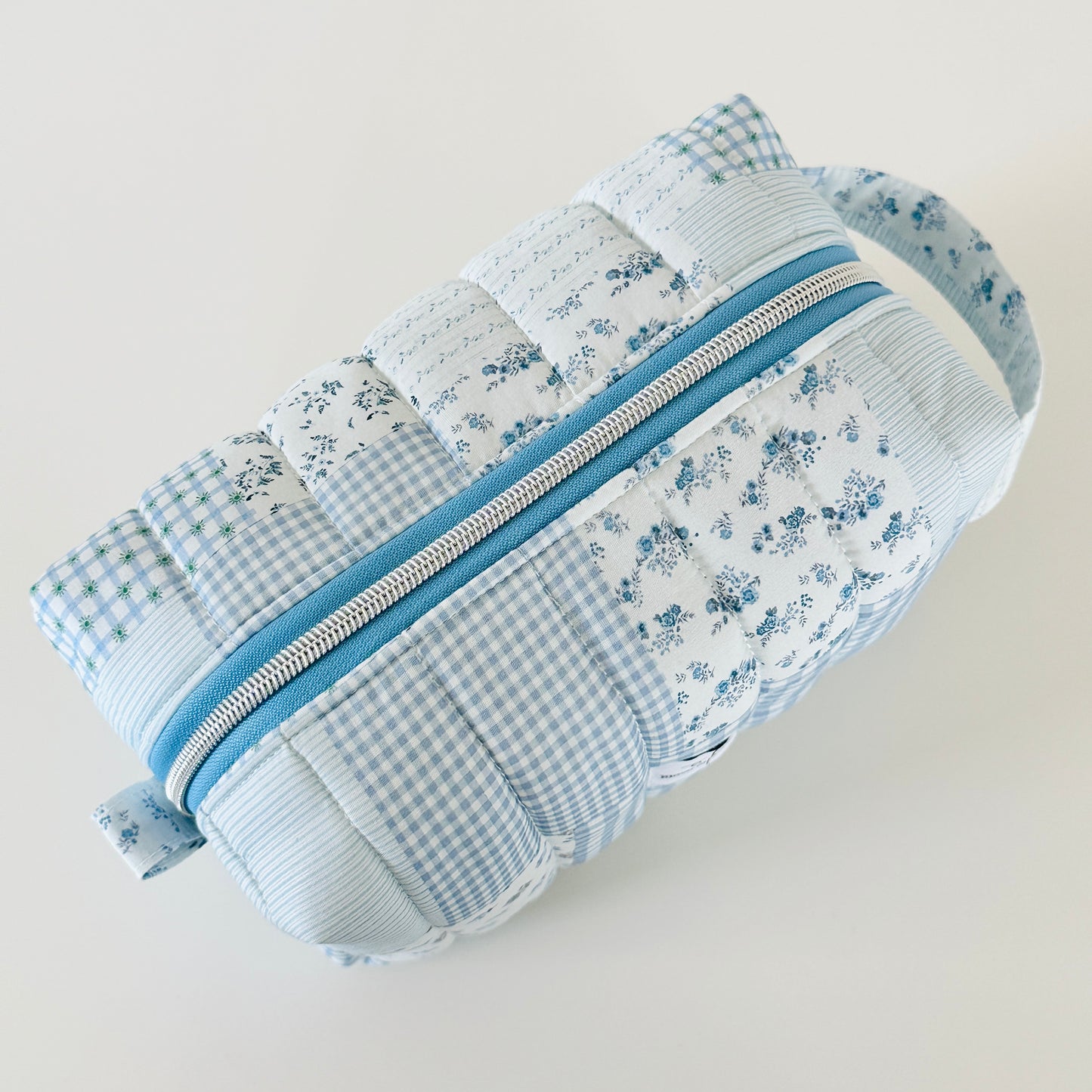 Patchwork pouch with floral and gingham patterns and a blue zipper on a light gray background