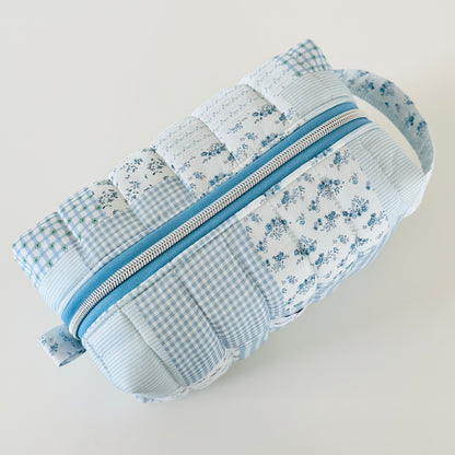 Patchwork pouch with floral and gingham patterns and a blue zipper on a light gray background