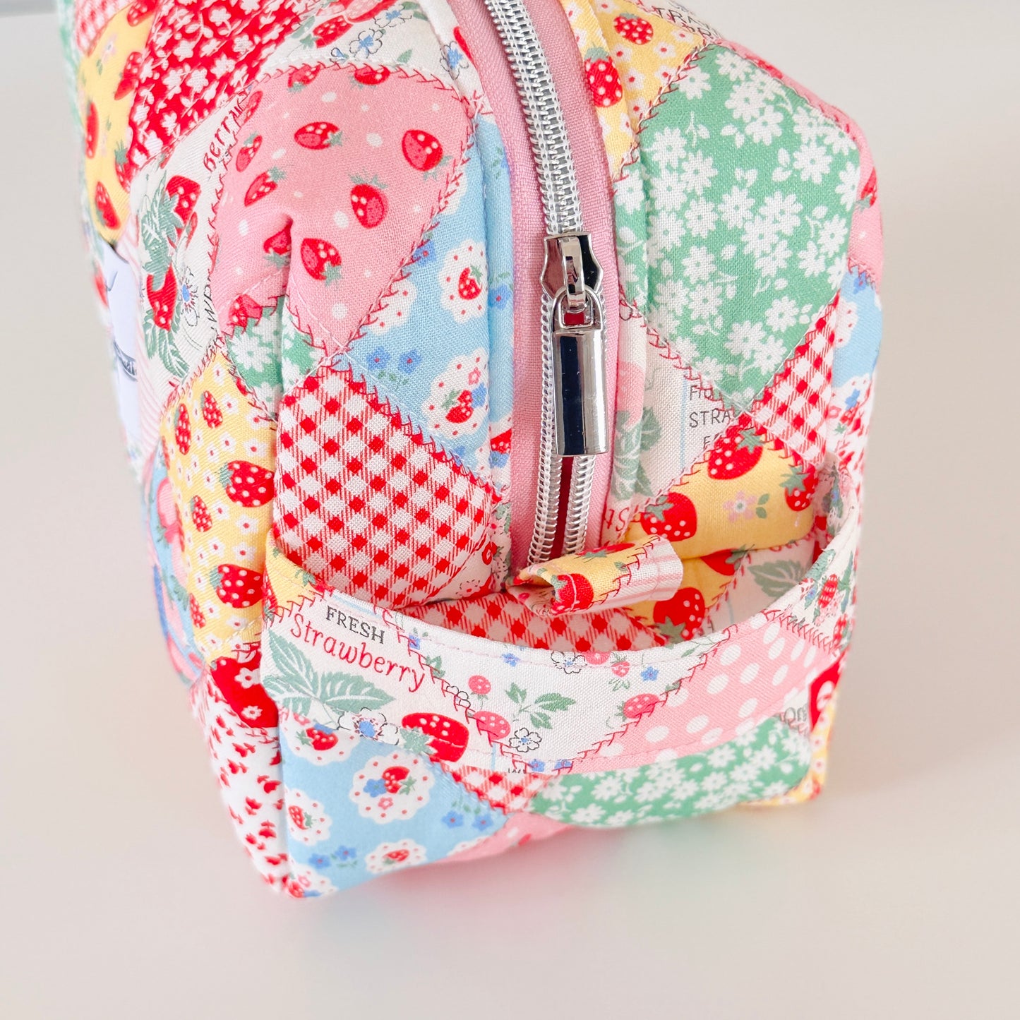 Patchwork-style fabric cosmetic bag with strawberry pattern on a light background