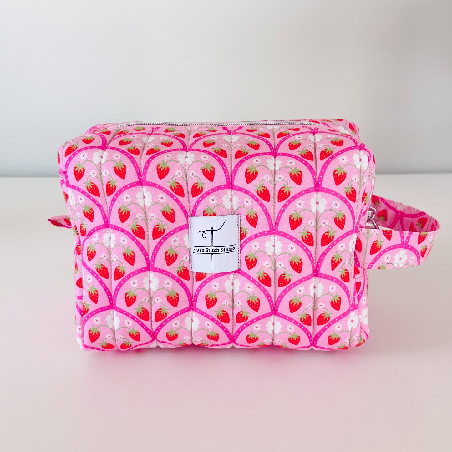 Pink makeup bag with strawberry pattern on a light gray background