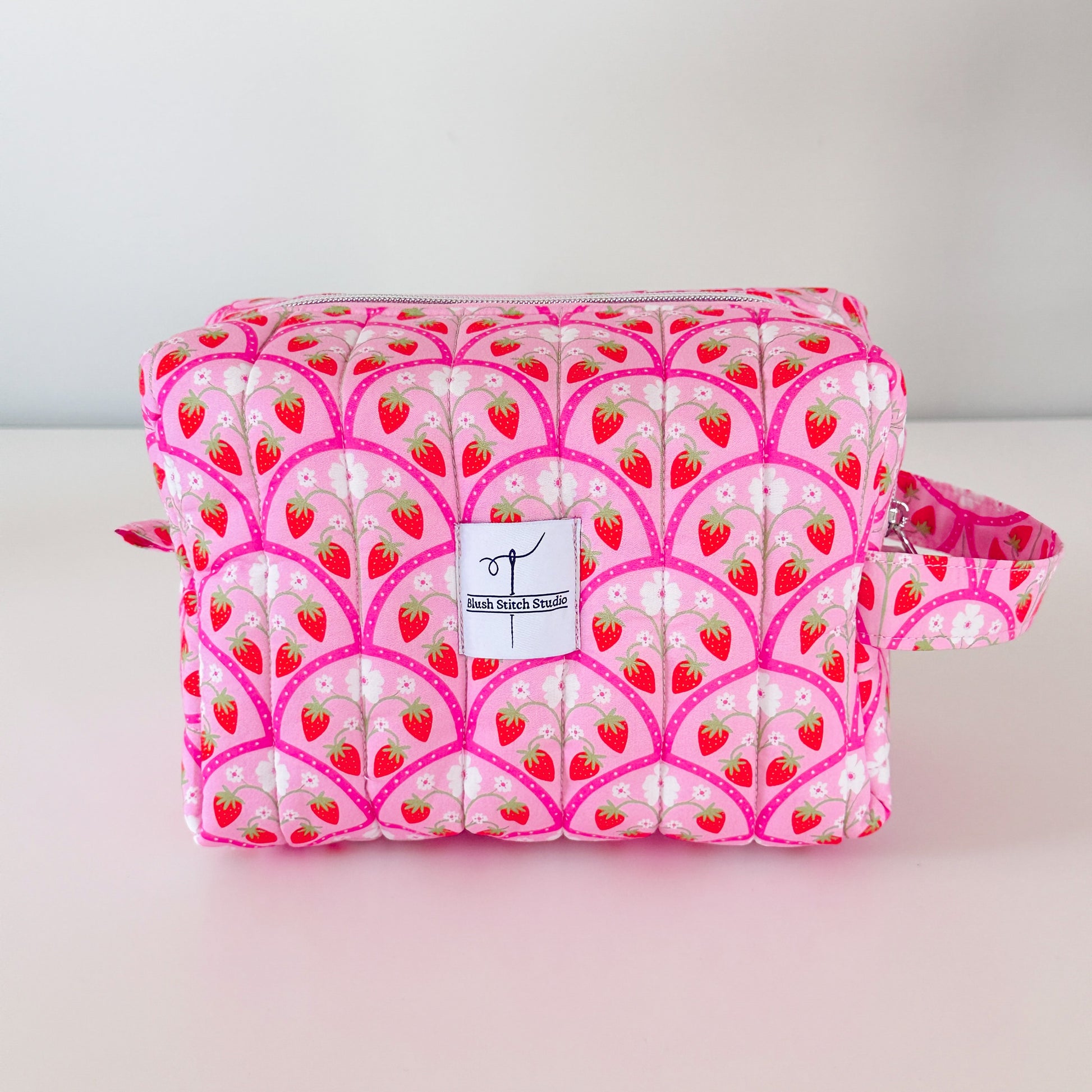 Pink makeup bag with strawberry pattern on a light gray background