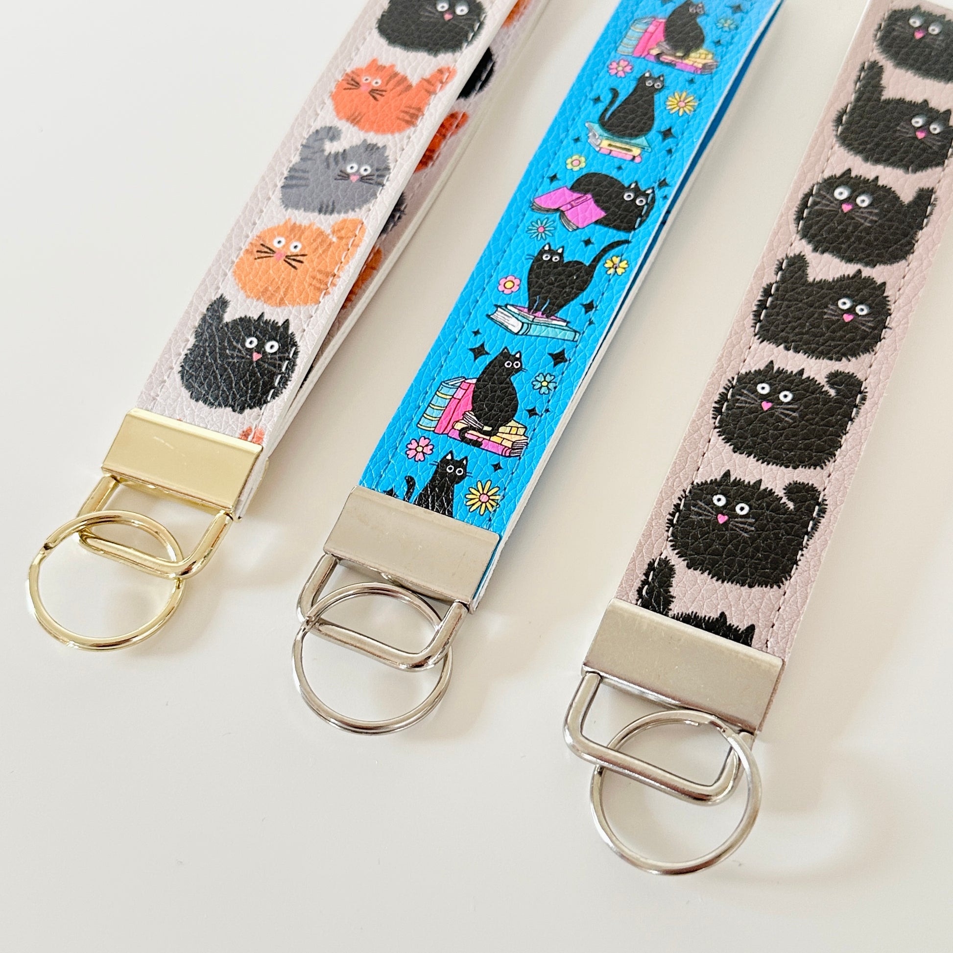 Three keychains with cat patterns on fabric straps against a white background
