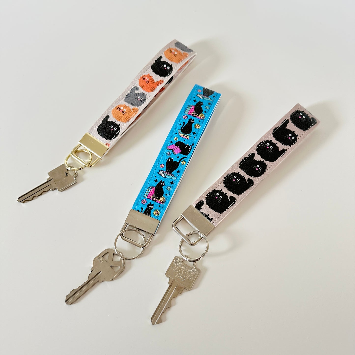 Three key wristlets with cat designs on a white background