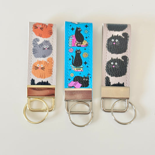 Three keychains with cat designs on a white background