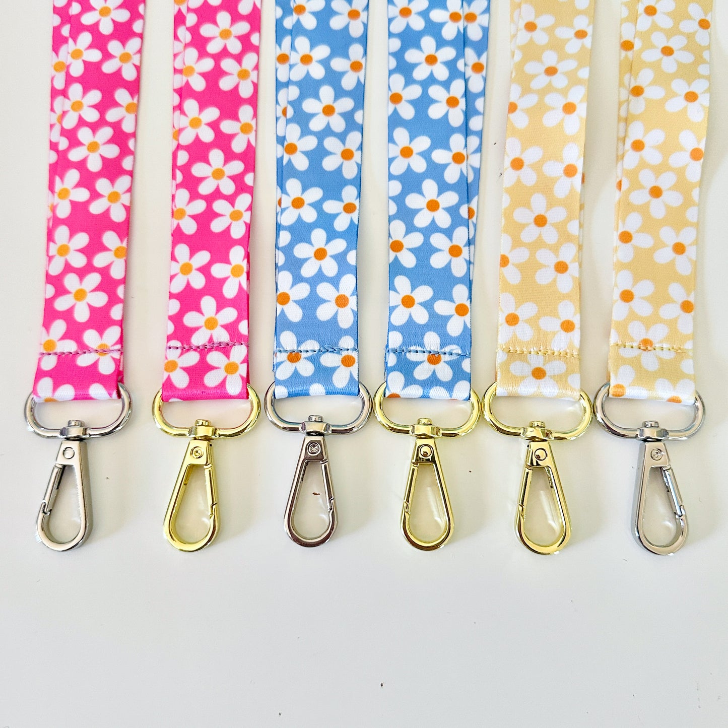 Four  daisy floral lanyards in pink, blue, and yellow on a white background