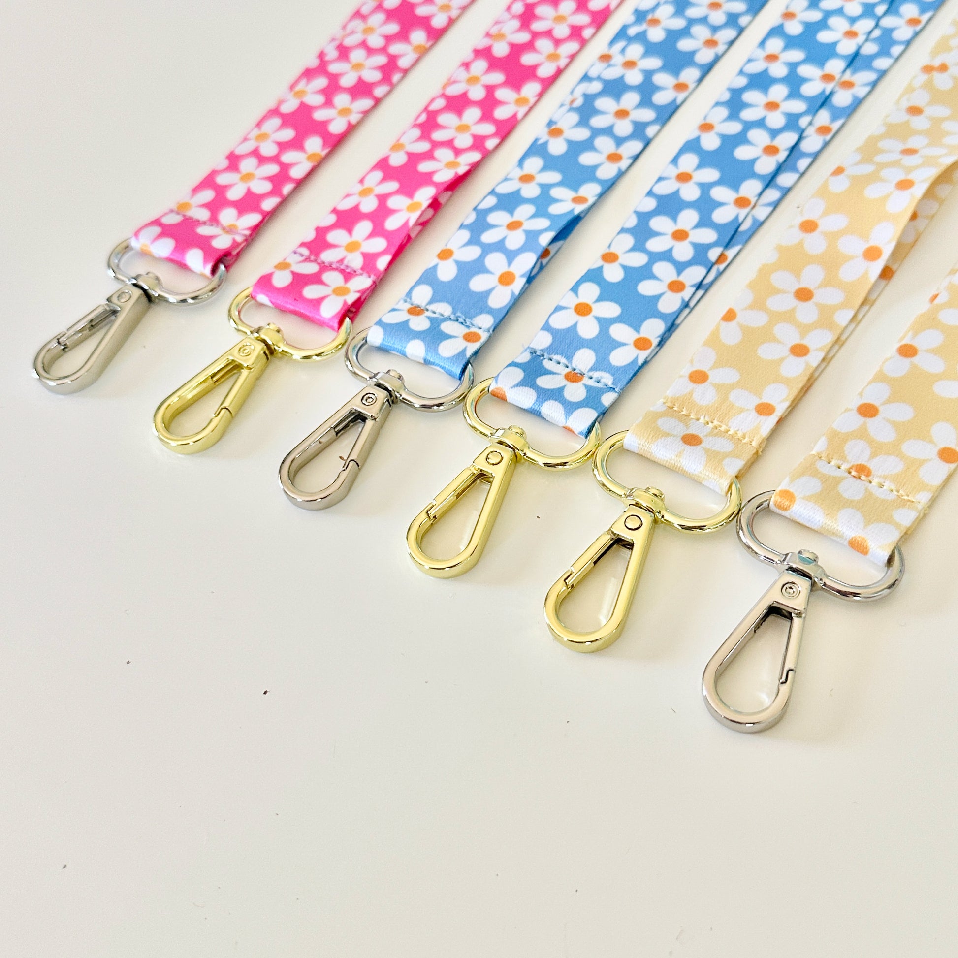 Four  daisy floral lanyards in pink, blue, and yellow on a white background