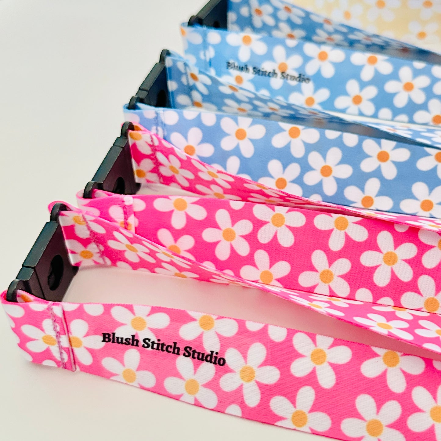 Four  daisy floral lanyards in pink, blue, and yellow on a white background