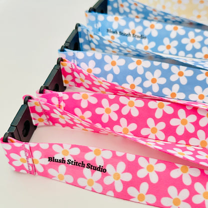 Four  daisy floral lanyards in pink, blue, and yellow on a white background