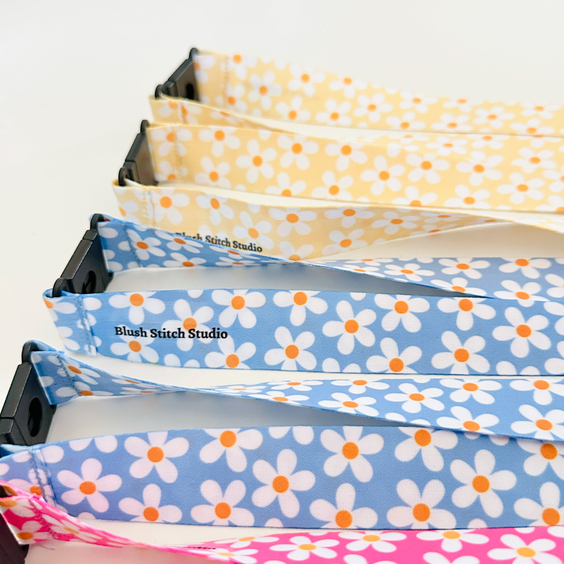 Four  daisy floral lanyards in pink, blue, and yellow on a white background