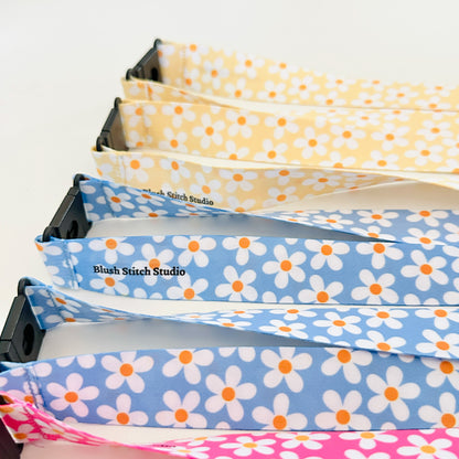 Four  daisy floral lanyards in pink, blue, and yellow on a white background