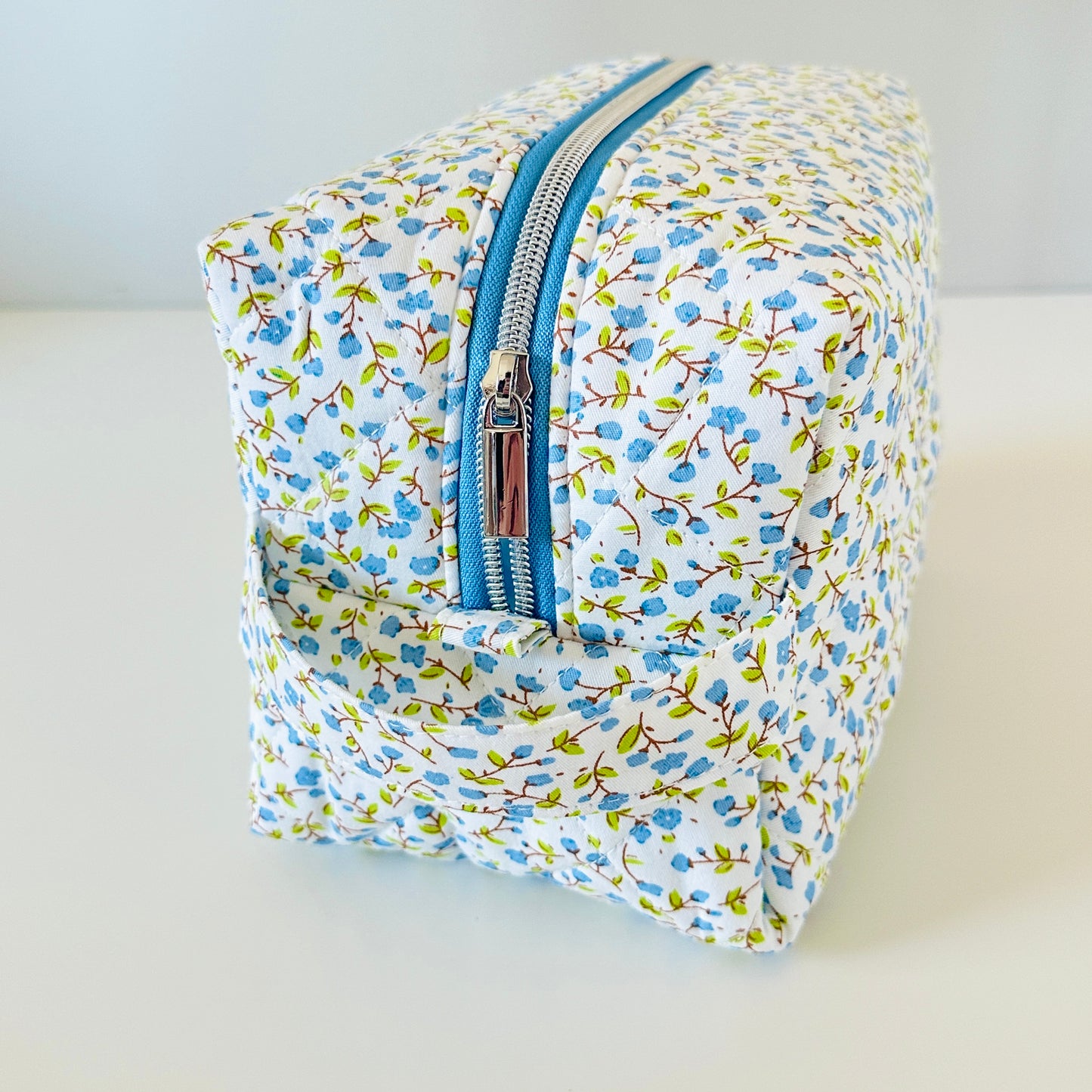 Floral-patterned toiletry bag with a blue zipper on a light background