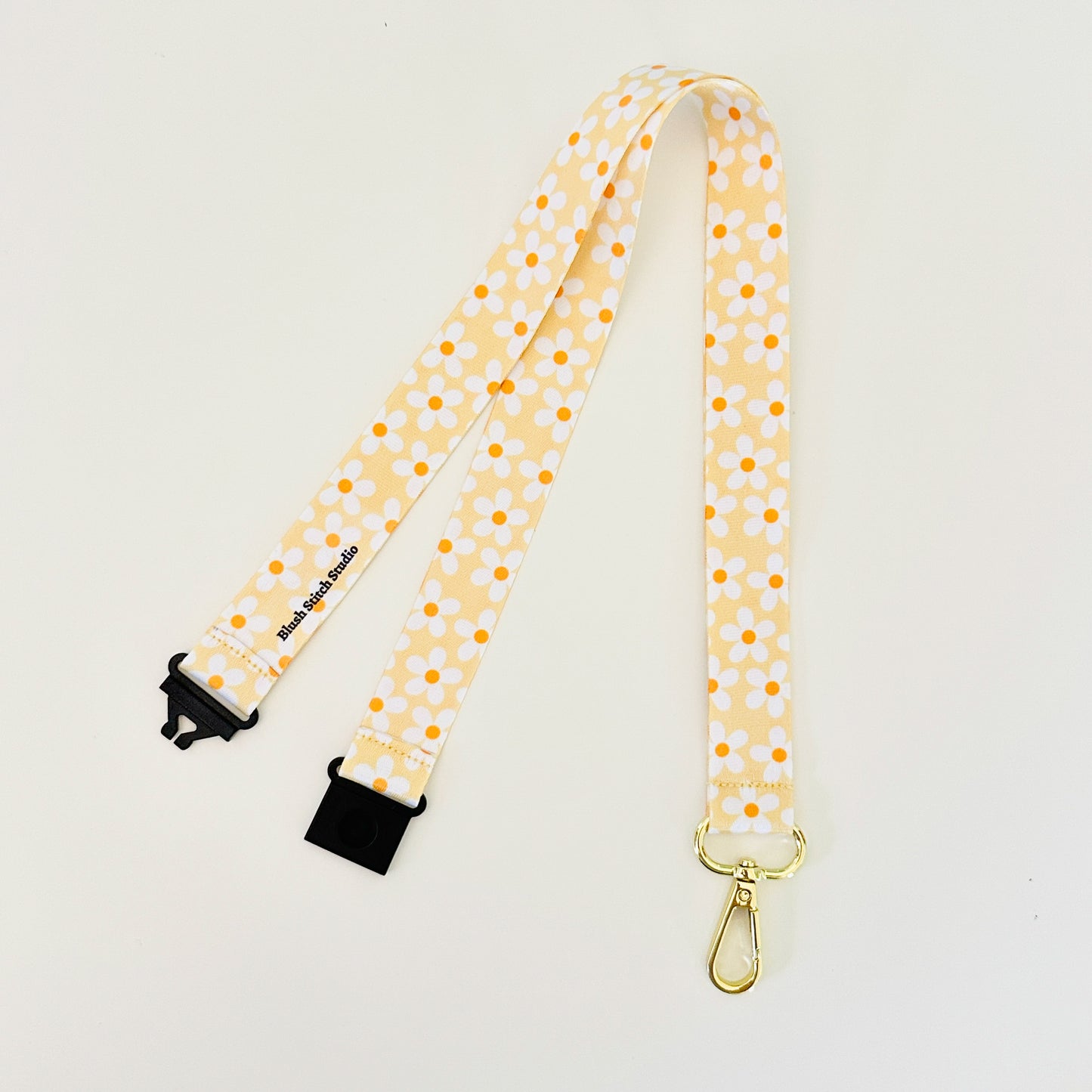 Yellow daisy floral lanyard with black clips on a light gray background