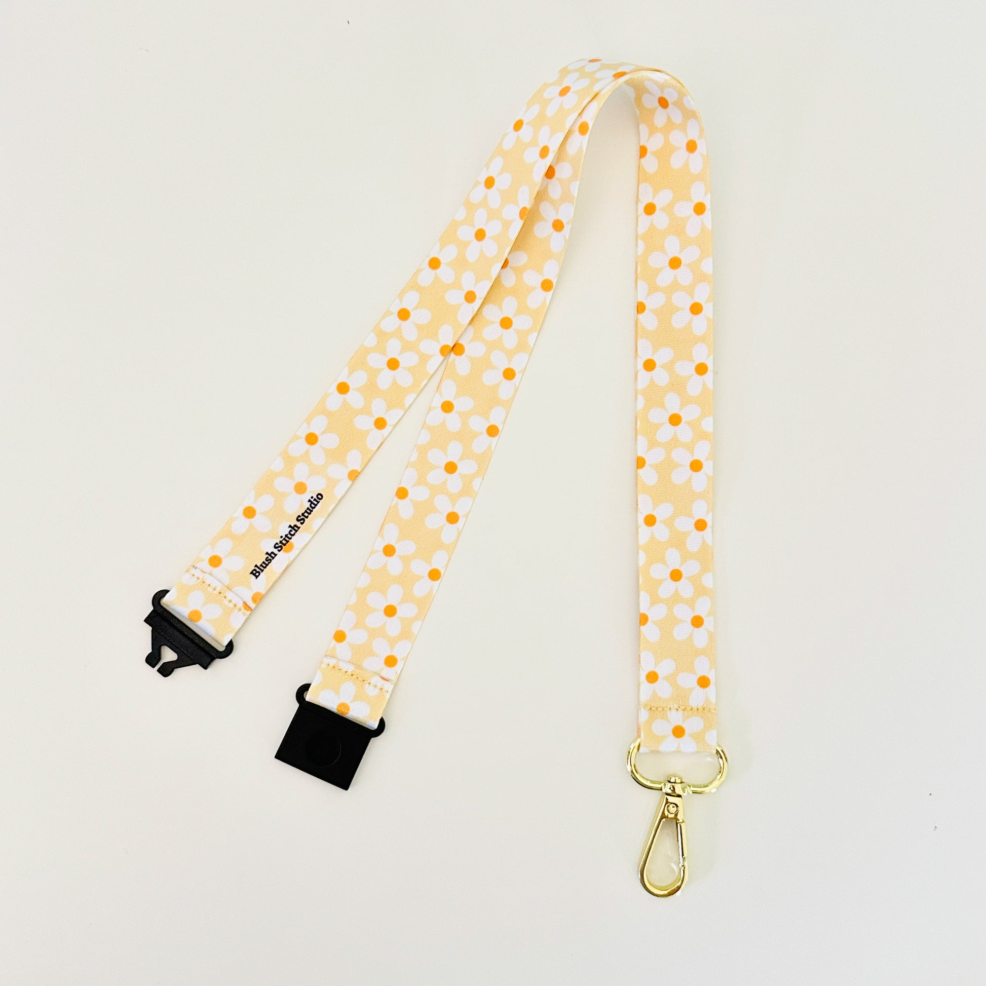 Yellow daisy floral lanyard with black clips on a light gray background