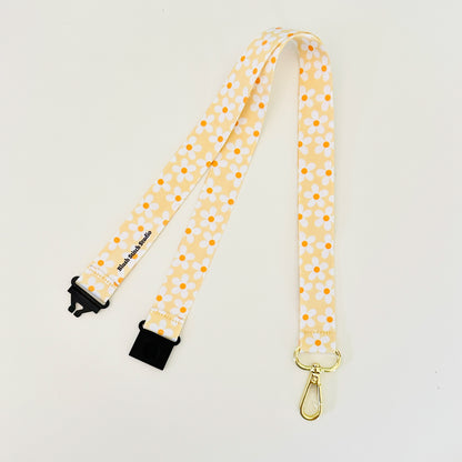 Yellow daisy floral lanyard with black clips on a light gray background