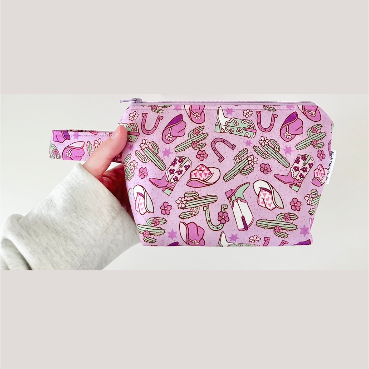 purple pouch with cactus, cowgirl hat and boot pattern held by a person on a light gray background