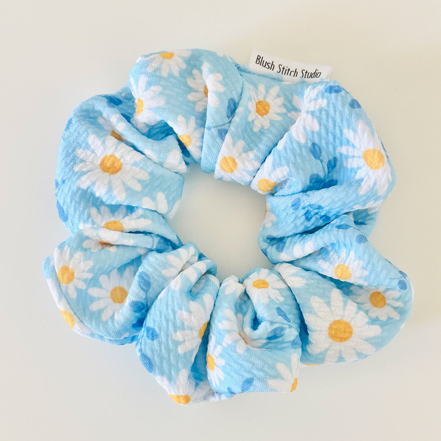 Blue scrunchie with white daisies and yellow centers on a light gray background