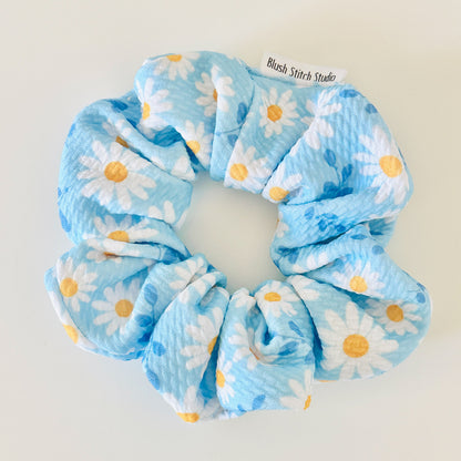 Blue scrunchie with white daisies and yellow centers on a light gray background