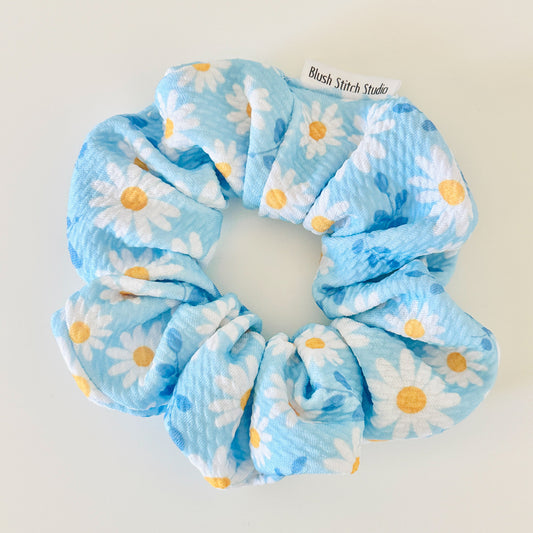 Blue scrunchie with white daisies and yellow centers on a light gray background