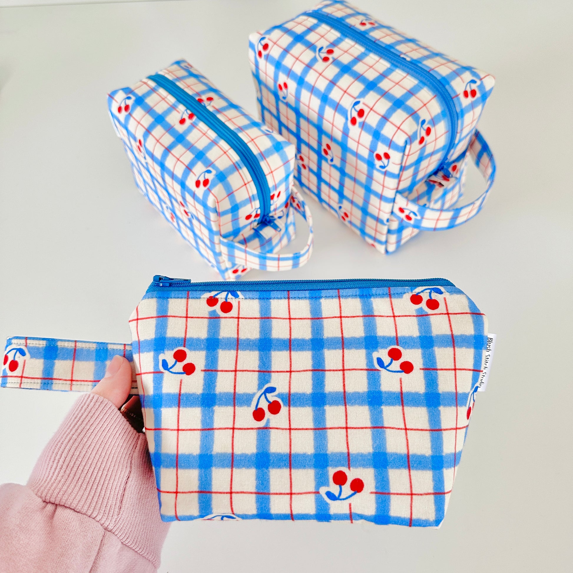 Set of three fabric pouches with blue plaid pattern and red cherries on a light gray background.
