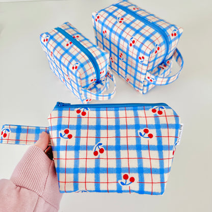 Set of three fabric pouches with blue plaid pattern and red cherries on a light gray background.