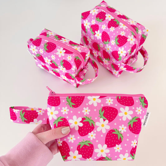Set of pink makeup bags with strawberry and flower pattern on a light background