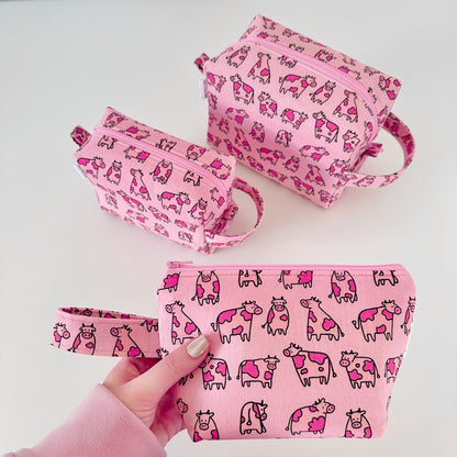 Set of pink bags with cow pattern held by a hand on a light gray background