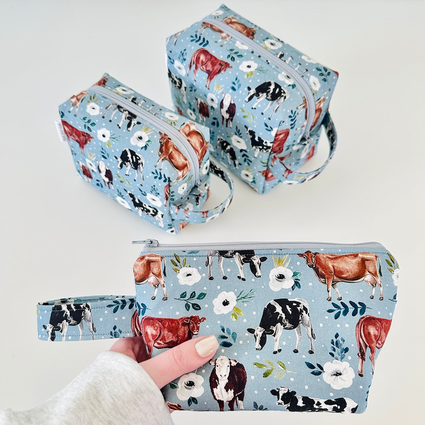 Set of three pouches with cow and floral pattern on a light blue background