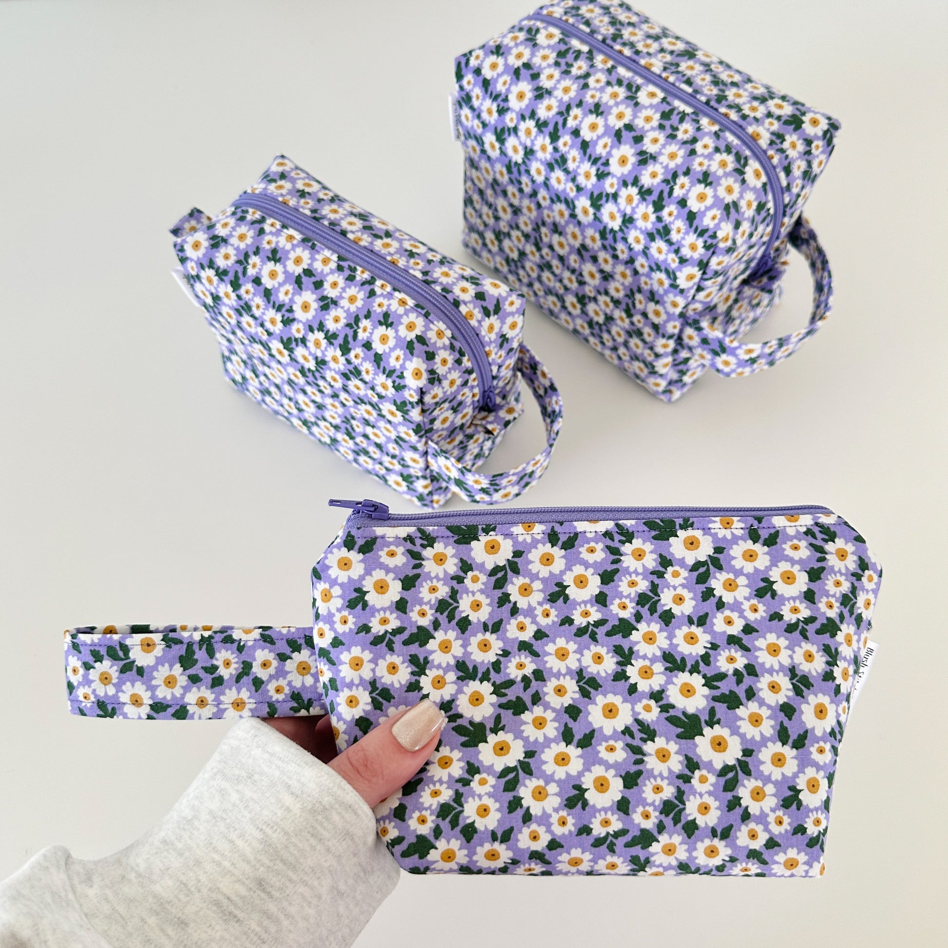 Set of floral-patterned pouches with a hand holding one of them on a light background