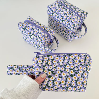 Set of floral-patterned pouches with a hand holding one of them on a light background