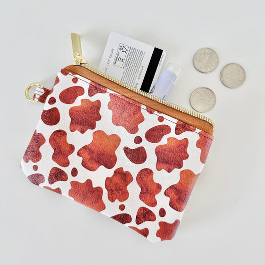Cow print coin purse with coins and cards on a white background