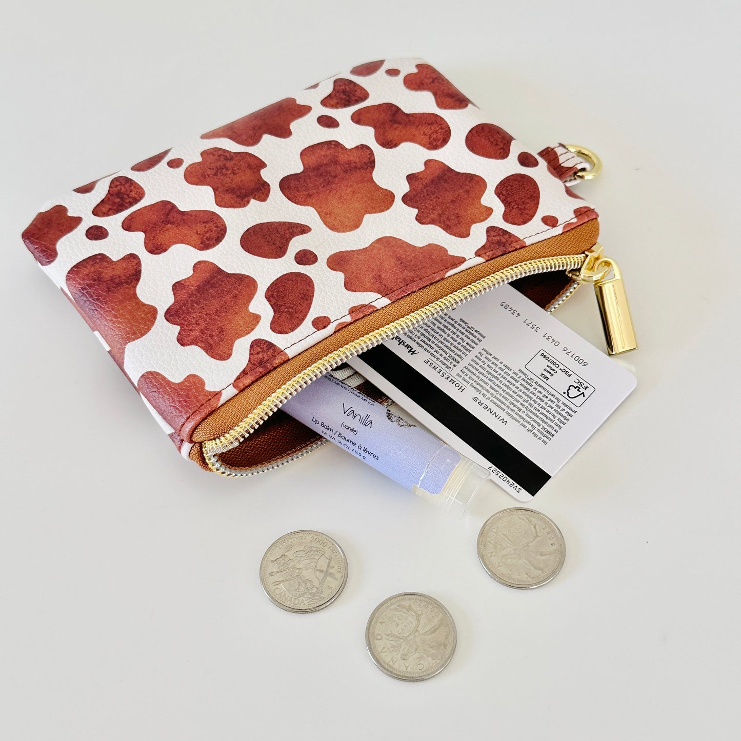 Cow print coin purse with coins and cards on a white background