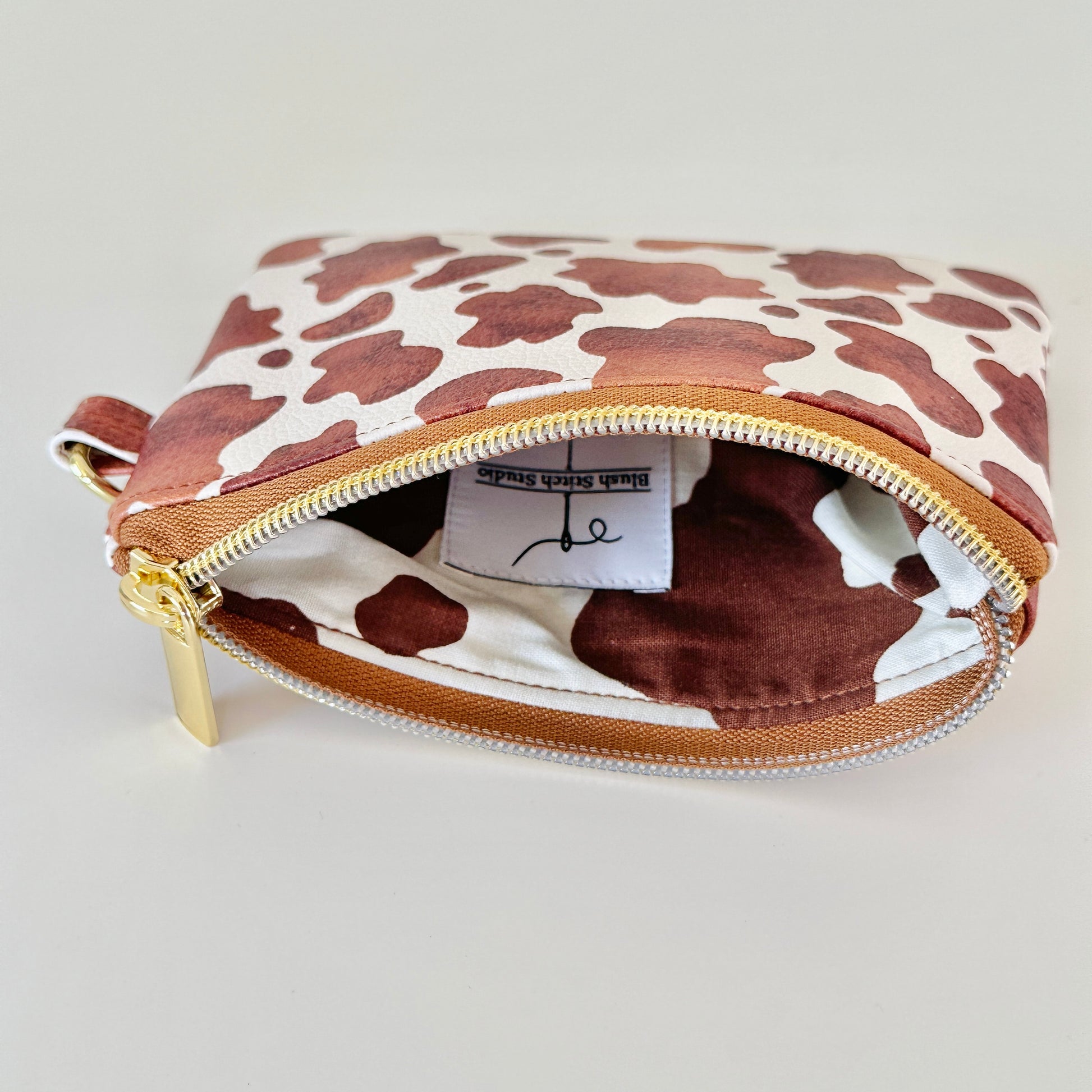 Cow print coin purse with coins and cards on a white background
