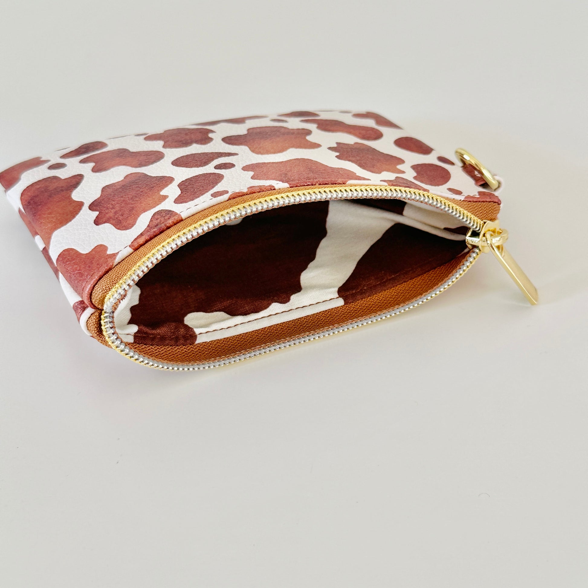 Cow print coin purse with coins and cards on a white background