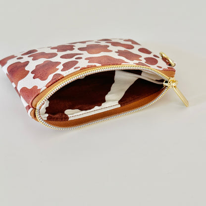 Cow print coin purse with coins and cards on a white background