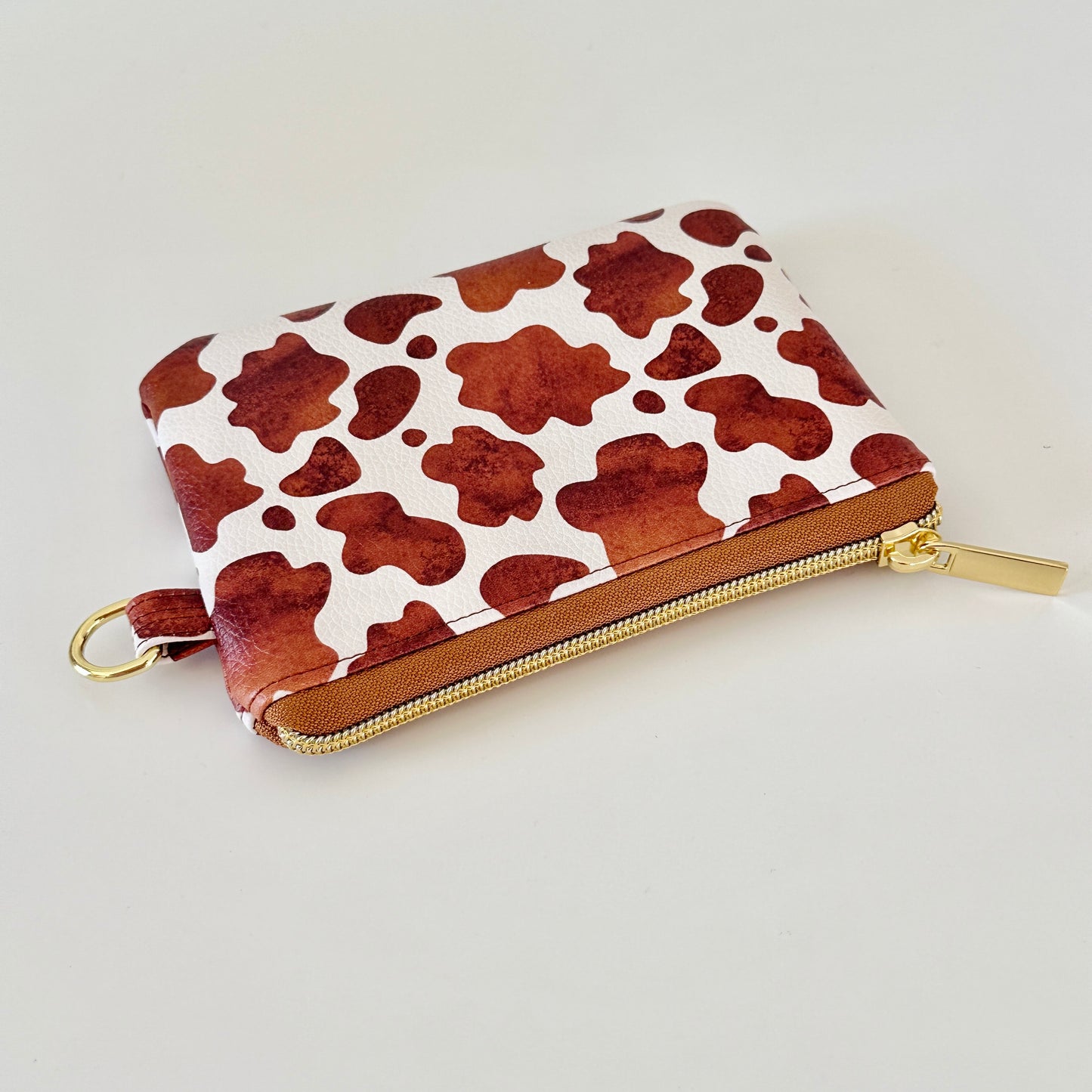 Cow print coin purse with coins and cards on a white background